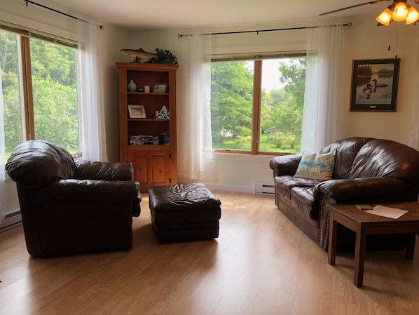 Un salon avec deux canapés en cuir, un meuble en bois et une grande fenêtre donnant sur un paysage verdoyant.