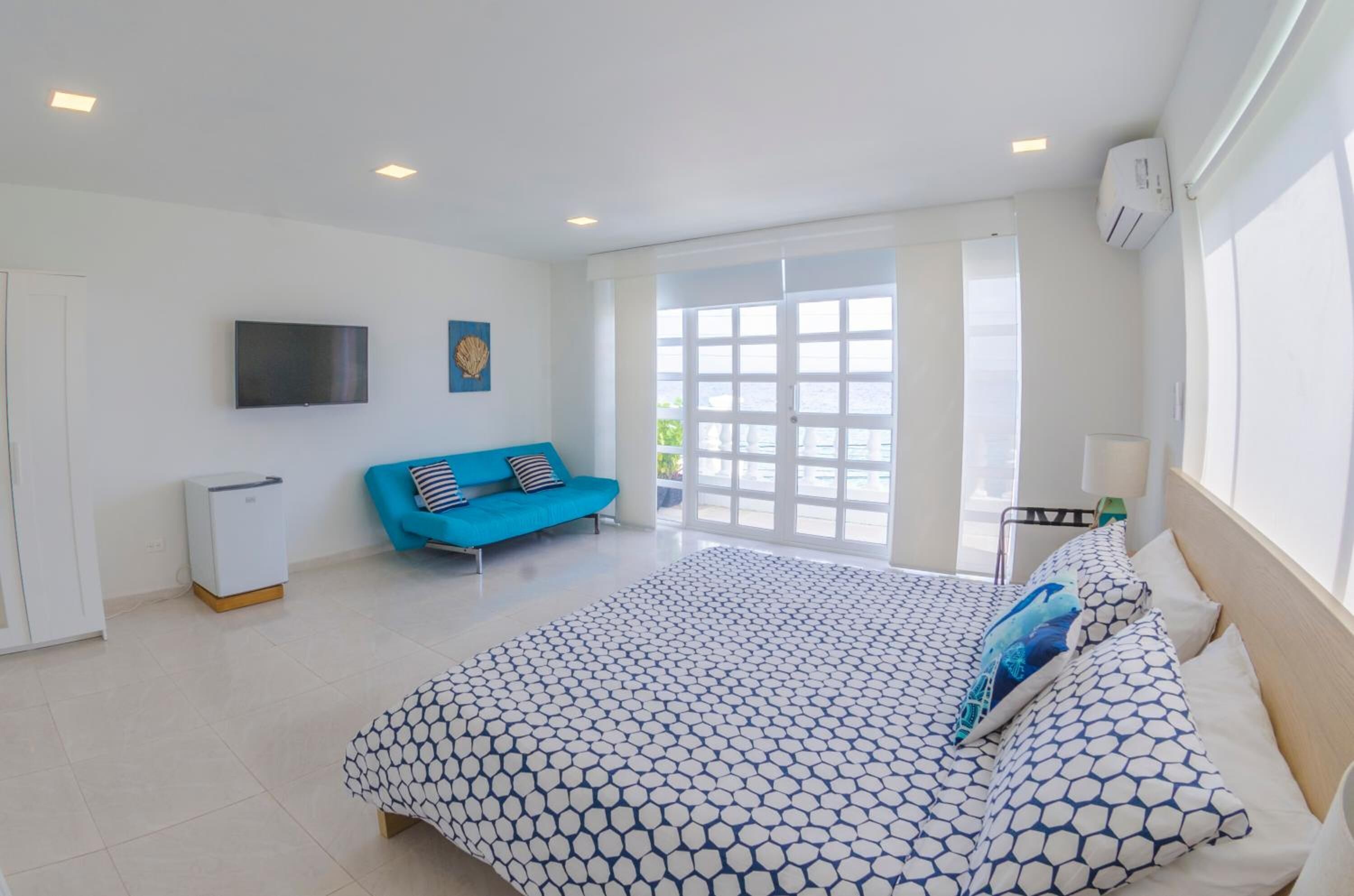 A bedroom with a bed, a blue sofa, a TV, and a large window.