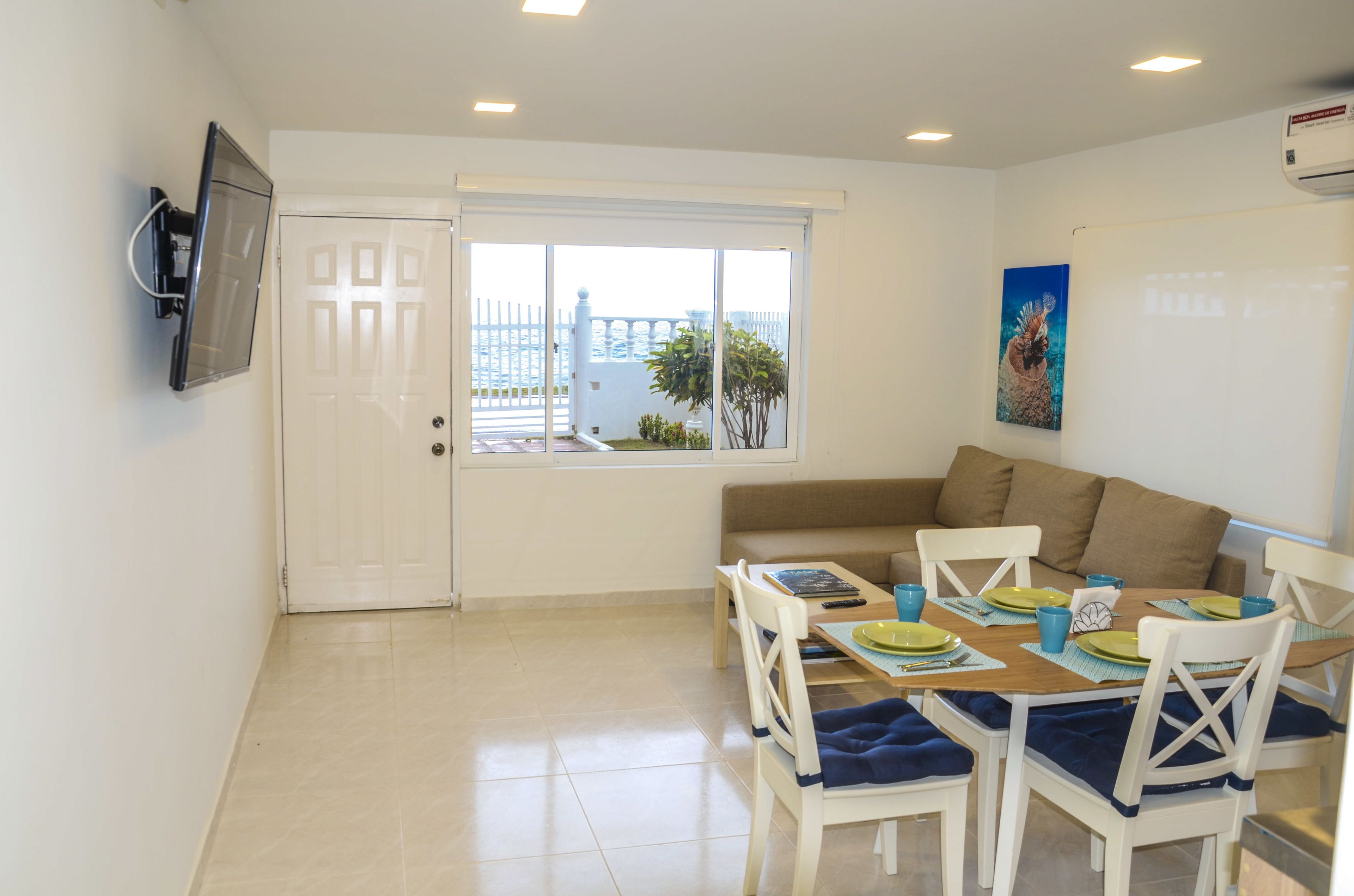 A dining area with a table set for four, white chairs, and a sofa.