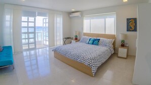 Un ampli dormitori amb un llit gran, un sofà blau i un balcó amb vista al mar.