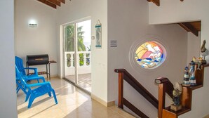 Habitació amb sostre de fusta, una cadira blava, una graella, una porta de vidre que dona a l'exterior i una finestra de vitrall.