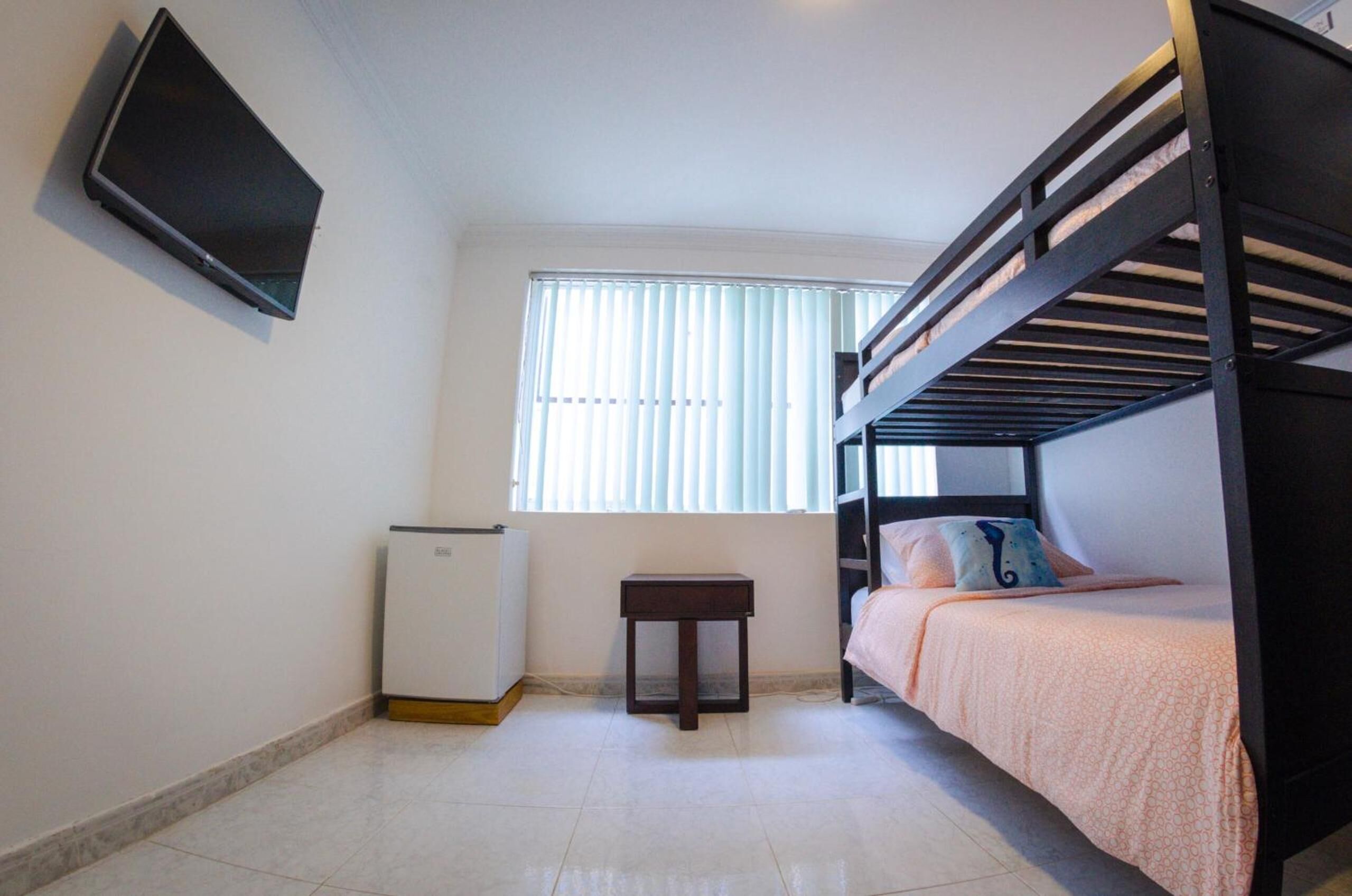 A small, clean room with a bunk bed, a small table, and a TV mounted on the wall.