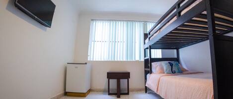 A small, clean room with a bunk bed, a small table, and a TV mounted on the wall.