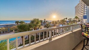A balcony with a view of the ocean and beach, a pool area, and a building with balconies.