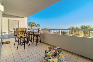 A balcony with a white door, two chairs with floral upholstery, a small table, and a view of the sea.
