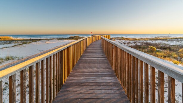A wooden boardwalk leading to a beach with a flag at the end.