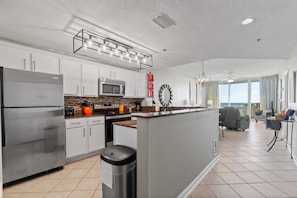 A modern kitchen with stainless steel appliances, a central island, and a dining area with a view. - Beach Club B309-Bristol - Beach Front (Gulf Shores)