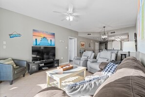 A living room with a TV, sofa, armchair, coffee table, and a painting of a sunset over a pier.