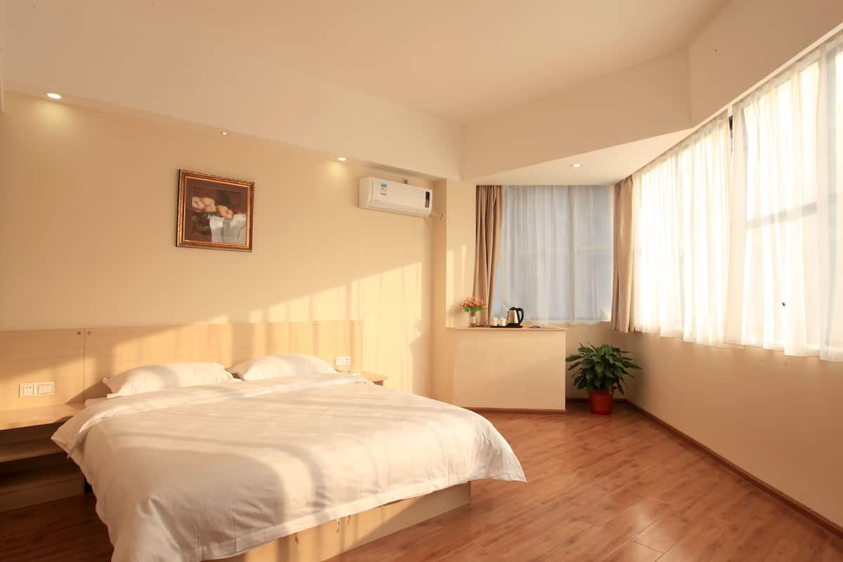 Un dormitorio con cama, ventana con cortinas, planta en maceta y unidad de aire acondicionado en la pared.