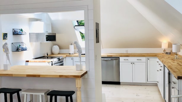 Une cuisine moderne avec des meubles blancs, un plan de travail en bois et une lucarne.