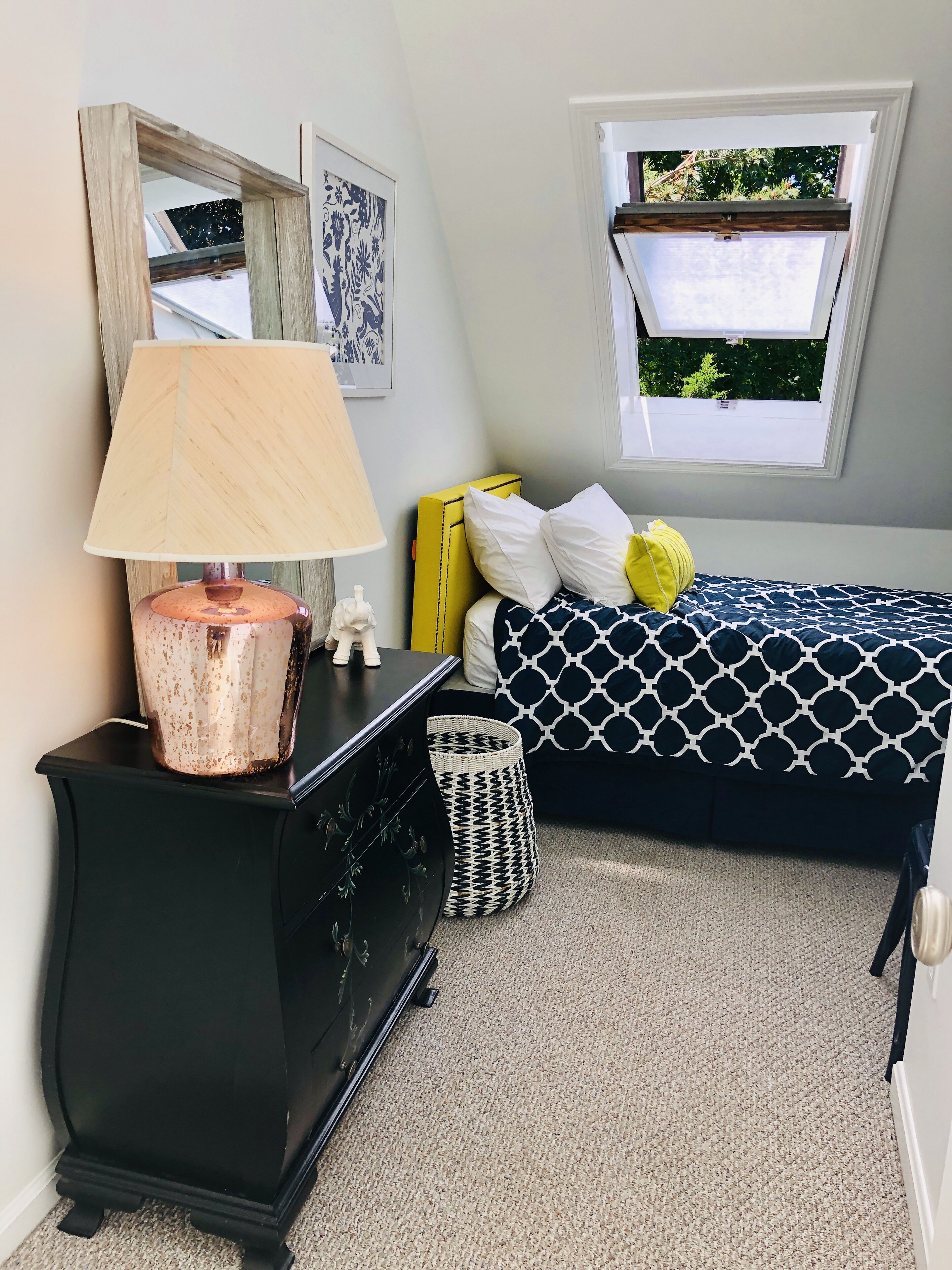 A bedroom with a bed, a nightstand, a lamp, a window, and a mirror.