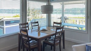 Un comedor con una mesa y sillas de madera, una lámpara y vistas a un paisaje urbano a través de amplios ventanales.