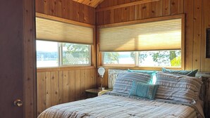 Un dormitorio con paneles de madera, una cama, dos mesitas de noche y una ventana con persianas.