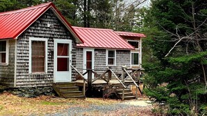 A rustic cabin with a red roof and wooden exterior, surrounded by dense forest. - Hobby Horse - Rustic Maine Cabin, Ocean Access 22 miles from Acadia Nat'l Park (Surry)