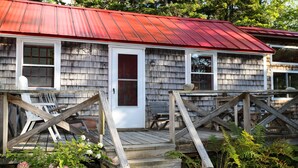 A wooden house with a red roof, a front porch with a bench, and a wooden staircase leading to the door. - Hobby Horse - Rustic Maine Cabin, Ocean Access 22 miles from Acadia Nat'l Park (Surry)