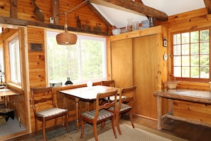 A wooden cabin interior with a dining table, four chairs, a window, and a door. - Hobby Horse - Rustic Maine Cabin, Ocean Access 22 miles from Acadia Nat'l Park (Surry)