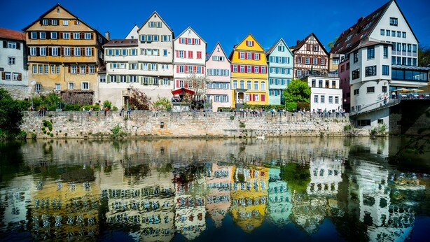 Een rij kleurrijke traditionele gebouwen langs een rivier, die zich in het water spiegelen.