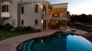 Una casa a due piani con piscina, area relax esterna e un giardino curato.