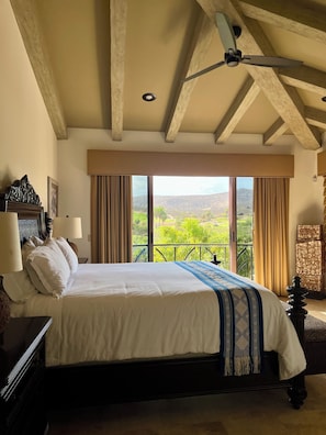 Een slaapkamer met een groot bed, een plafondventilator, uitzicht op de omgeving en een balkon.