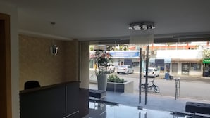 En modern entréhall med en receptionsdisk, en stor krukväxt och utsikt över gatan utanför.