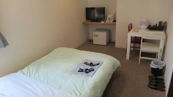A hotel room with a bed, a desk with a computer, a television, and a trash bin.