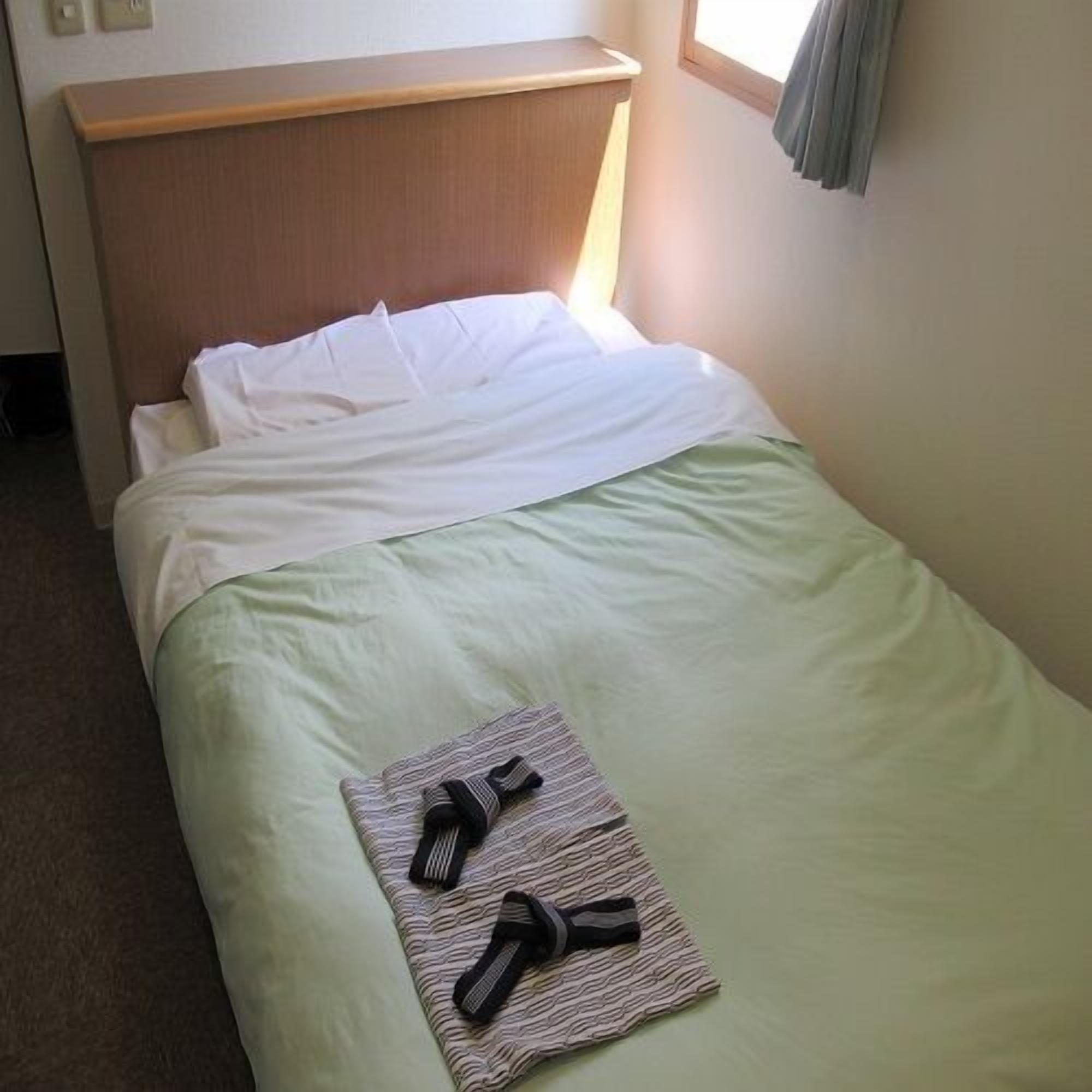 A single bed with a wooden headboard, a green bedspread, and a folded towel with black stripes on the foot of the bed.