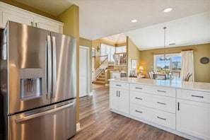A kitchen with a stainless steel refrigerator, white cabinetry, and a wooden floor. - The Taverner at Ships Watch in Duck - Great Semi-Ocean Front Property (Duck)