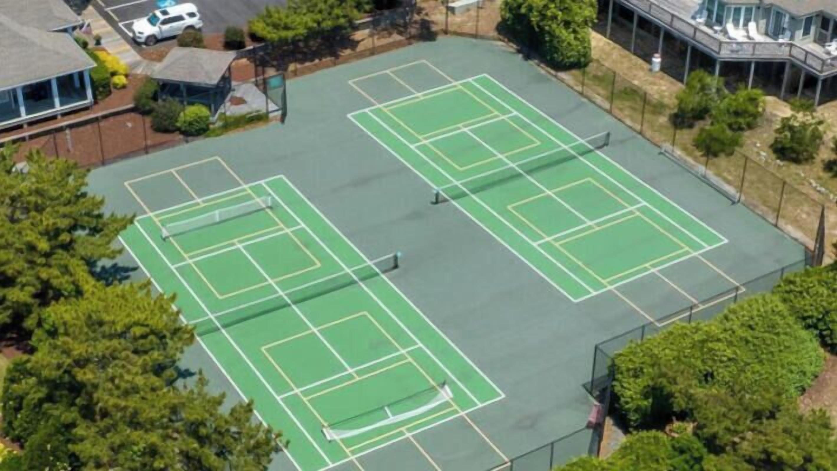 Vista aérea de un complejo de canchas de tenis con varias canchas, rodeado de árboles y edificios.