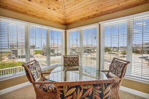 A glass-top table with wicker chairs in a room with large windows. - The Taverner at Ships Watch in Duck - Great Semi-Ocean Front Property (Duck)