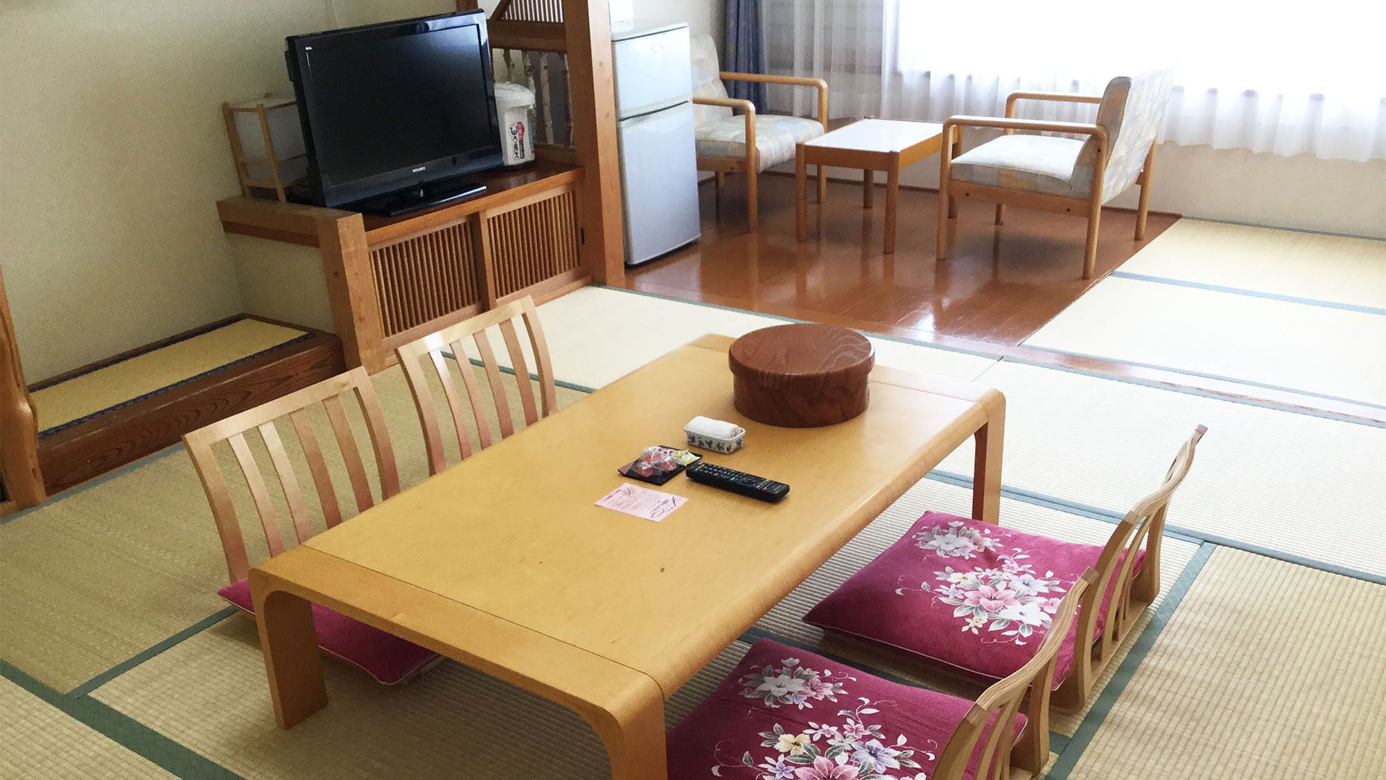 Een traditionele Japanse kamer met tatami vloerbedekking, een houten tafel, stoelen, een televisie en een koelkast.