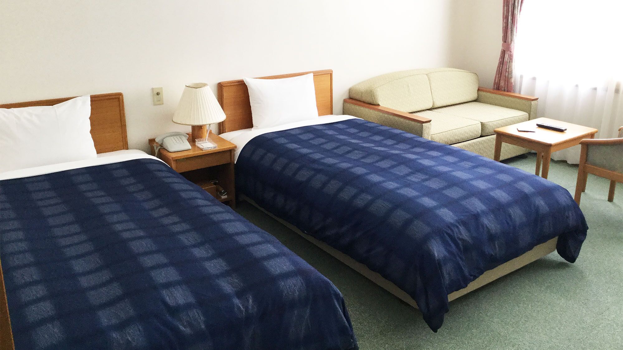 Een hotelkamer met twee bedden, een stoel, een klein tafeltje, een lamp en een telefoon.