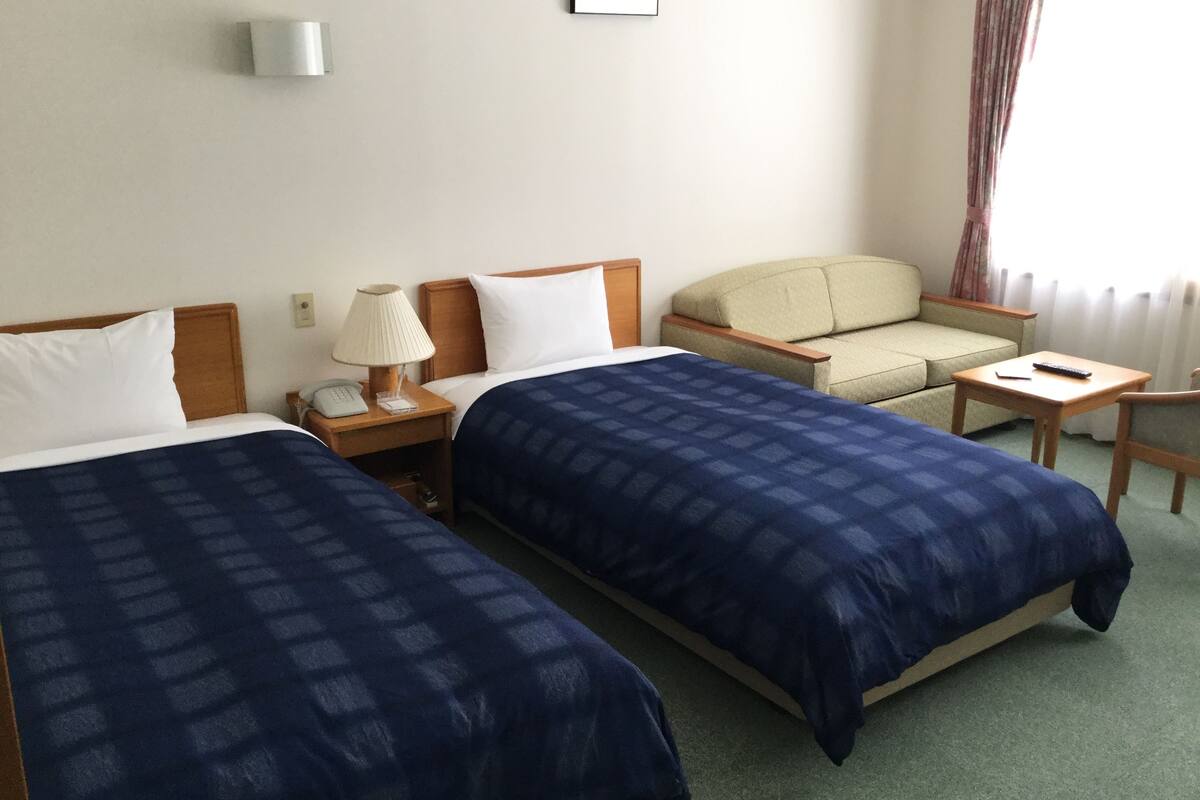 A hotel room with two beds, a sofa, a small table, and a lamp.