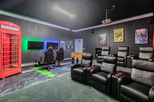 A home theater room with a red telephone booth, gaming chairs, and a projector screen. - 2022 Award @ Hosthub, Home Theater/Game Room/Harry Potter Rm Close to Disney (Reunion)