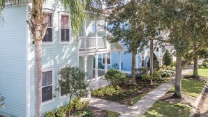 A light blue two-story house with a porch, surrounded by trees and a well-maintained lawn. - 2022 Award @ Hosthub, Home Theater/Game Room/Harry Potter Rm Close to Disney (Reunion)