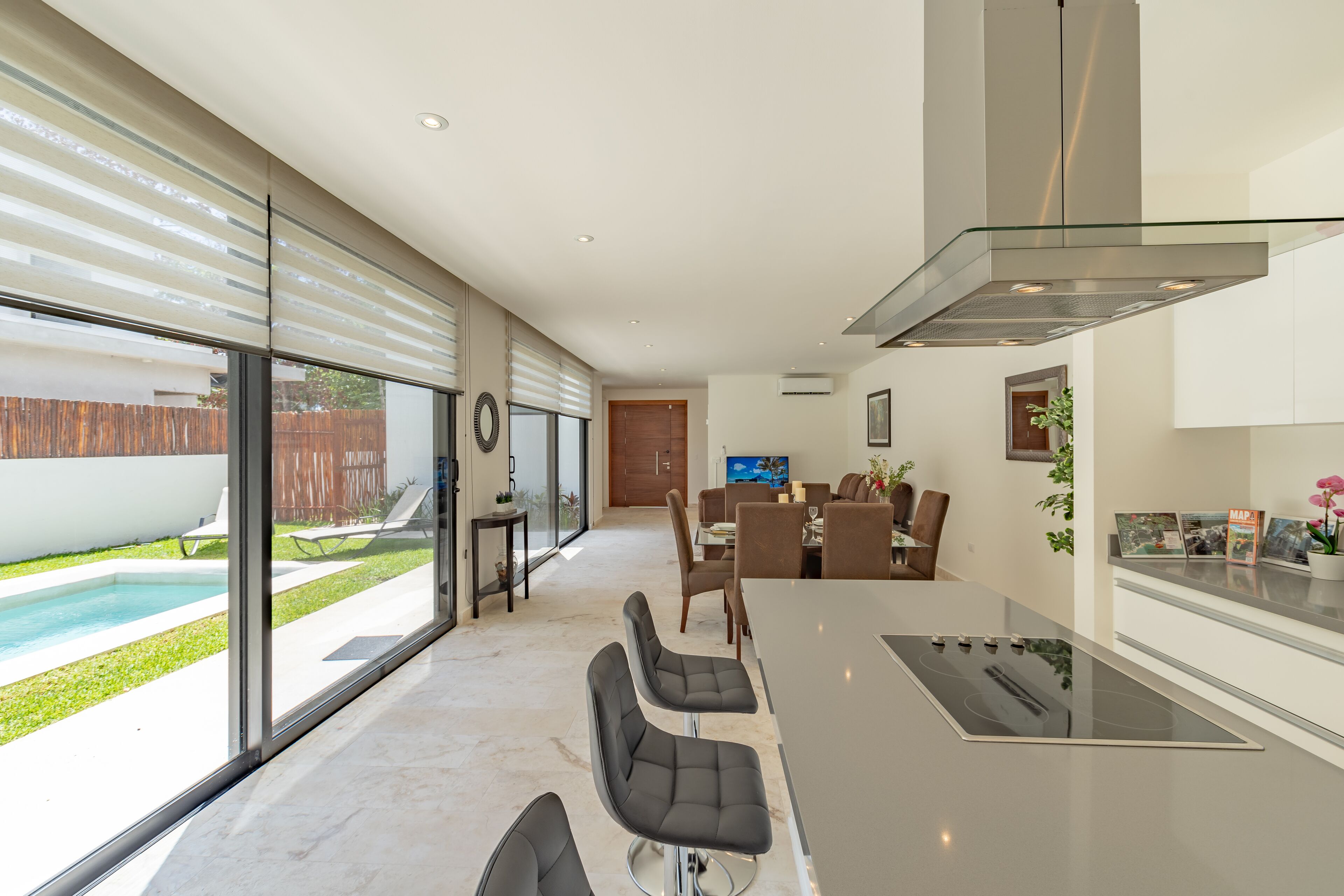 Une cuisine moderne dotée d’un grand îlot central, d’un coin repas avec des chaises et d’une vue sur une piscine.