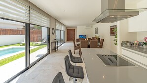Una cocina moderna con una isla grande, un comedor con sillas y vista a una piscina.