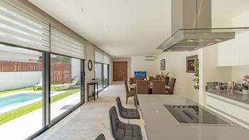 A modern kitchen with a large island, a dining area with chairs, and a view of a swimming pool.
