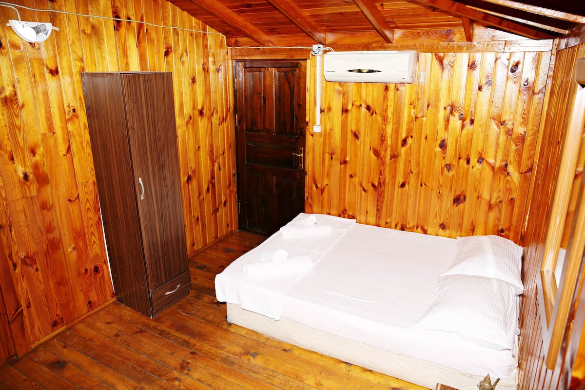 A wooden-paneled room with a bed, a wardrobe, and an air conditioning unit.