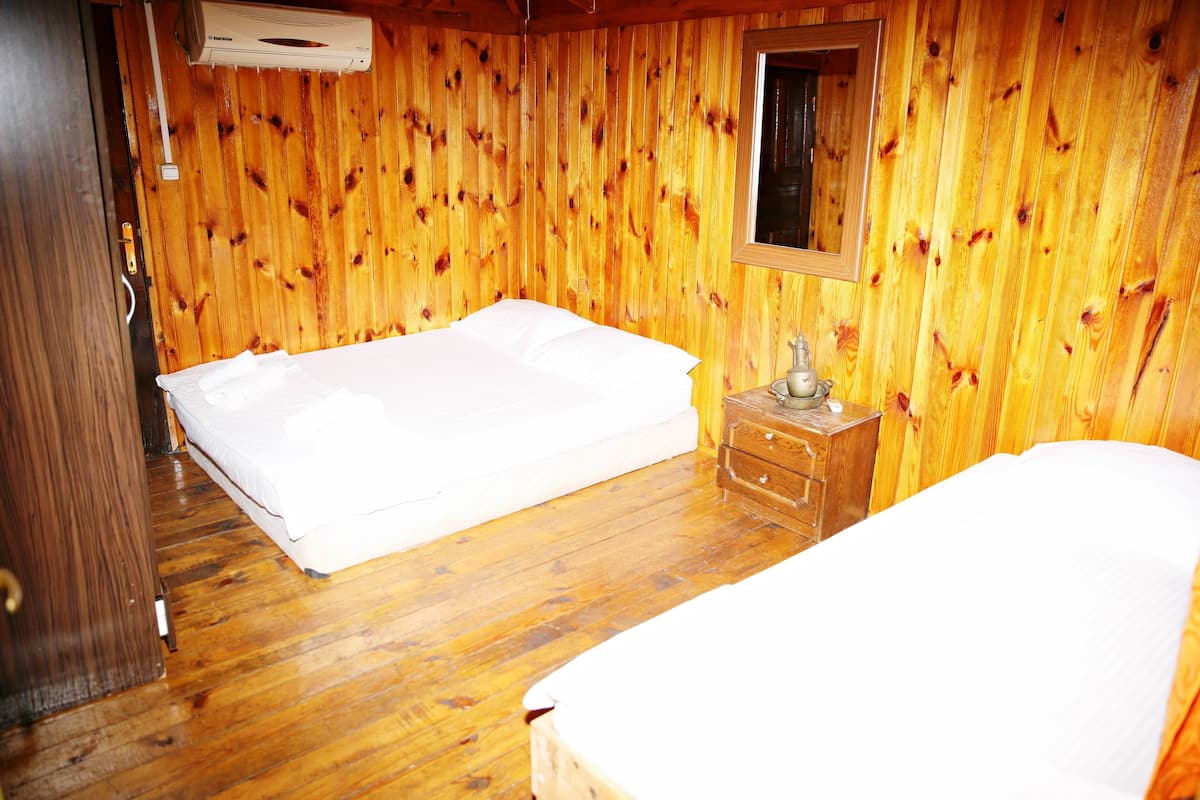 A wooden-paneled room with two beds, a wooden dresser, and a window.