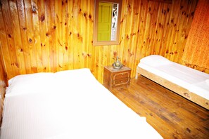 Een kamer met houten wanden en vloeren, twee bedden, een klein houten nachtkastje met een lamp en een spiegel aan de muur.