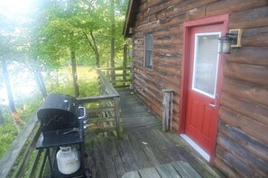 A wooden cabin with a red door, a small porch, and a grill outside.
