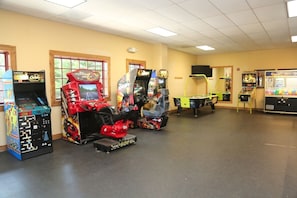 A room with arcade games, a pool table, and a projector screen.