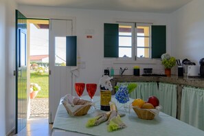 Een keuken met een tafel gedekt voor een maaltijd, een fles Madeira wijn en een mand met fruit.