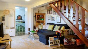 A cozy living room with a dark blue sofa, a wooden staircase, and a kitchen in the background. - Recanto das Florenças (1) – Great Views & Sunsets (Arco Da Calheta)