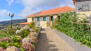 A house with a stone facade, a red-tiled roof, and a stone pathway leading to the entrance. - Recanto das Florenças (1) – Great Views & Sunsets (Arco Da Calheta)