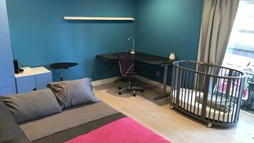 Een kamer met een bed, bureau, stoel, ledikant en raam met gordijnen.