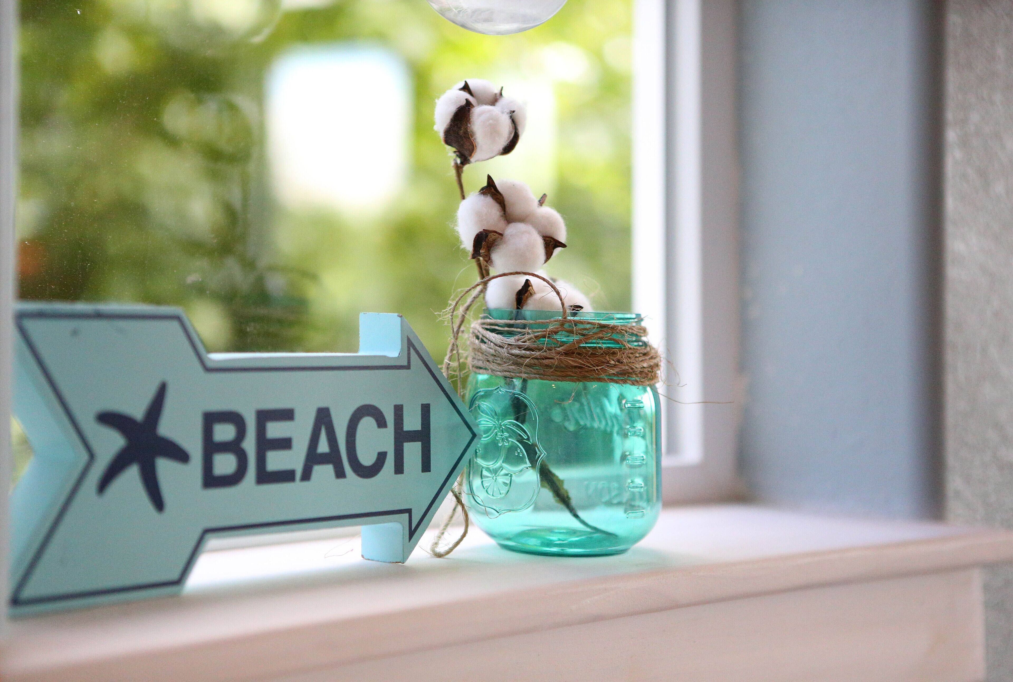 A sign with the word "BEACH" and a star, next to a jar with cotton bolls and twine.