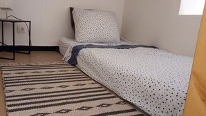 Une petite chambre à coucher, bien rangée, avec un lit simple, une table de chevet et un tapis.