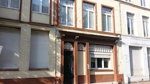 Un bâtiment à la façade marron et crème, orné d’une grande fenêtre au-dessus de l’entrée, dont le motif est en forme d’éventail, avec un volet fermé à gauche et un volet fermé à droite.