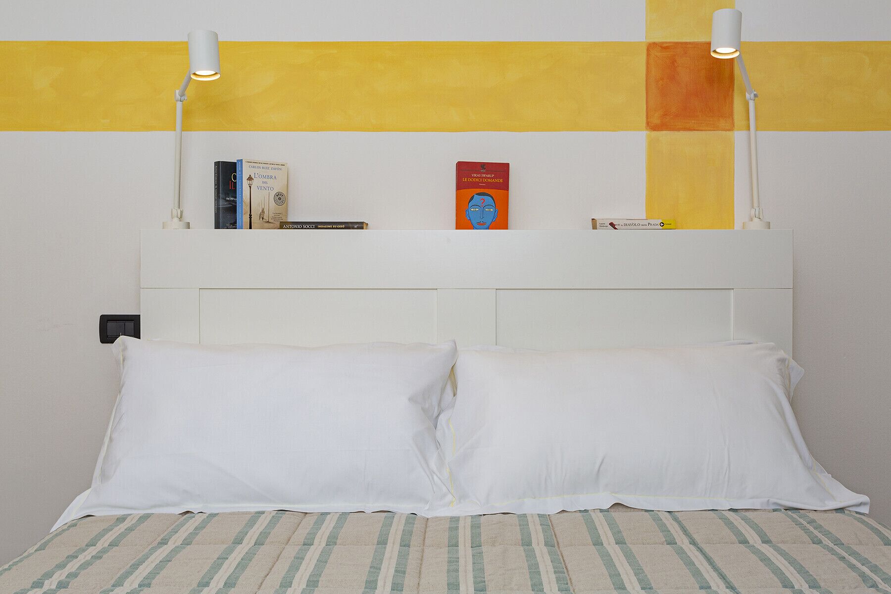 Ein Bett mit weißen Kissen, einer gestreiften Decke und einem weißen Kopfteil, sowie zwei Nachttischlampen.